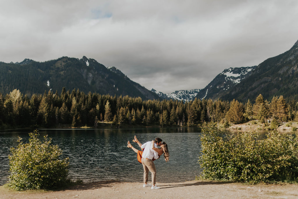 engagement-photos-couple-kisses-in-front-of-water-with-mountains-in-the-background