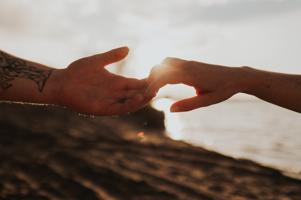 sand dunes in background, two people holding hands just by fingertips