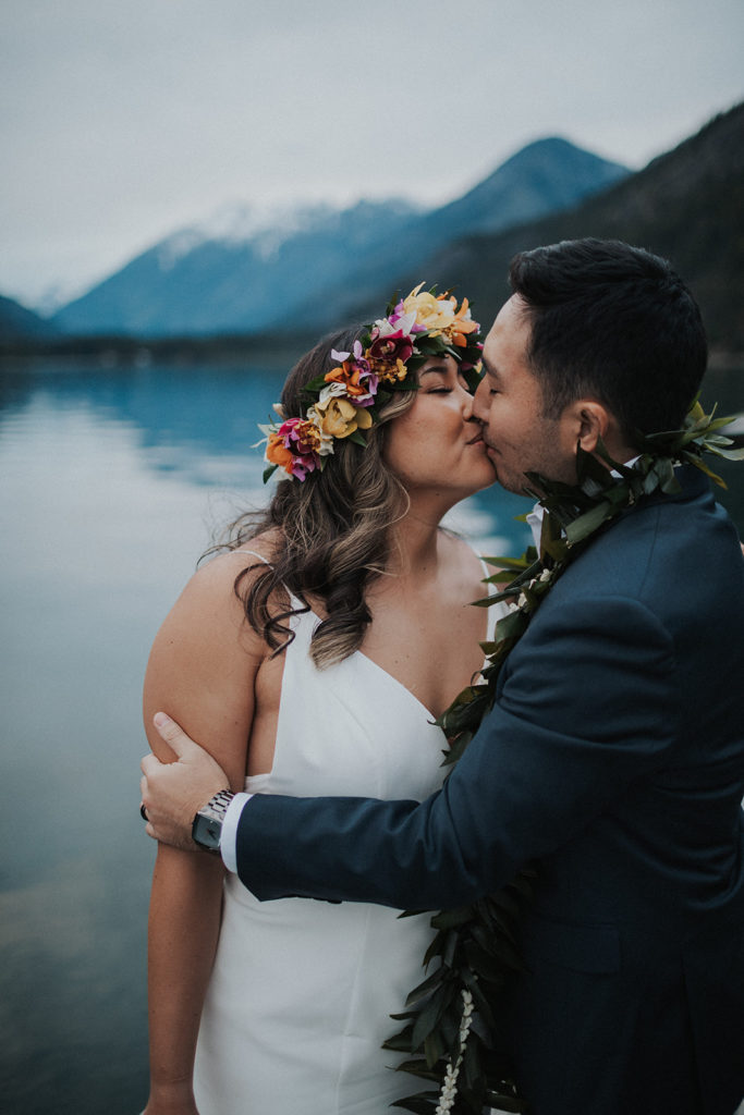 bride and groom kissing in front of lake and mountain national park elopement
