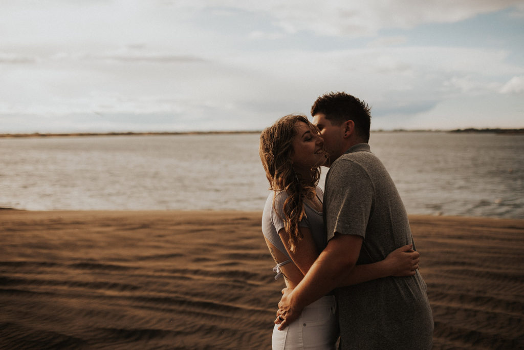 couple kissing at sand dunes with lake in the background
