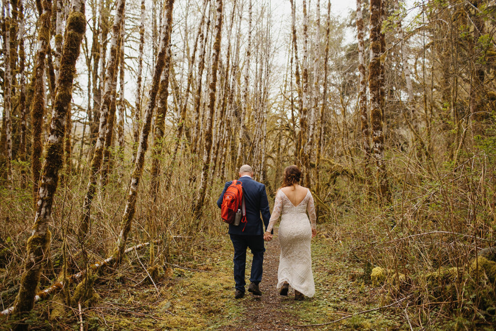 bride and groom walk through grove of trees during rain forest elopement