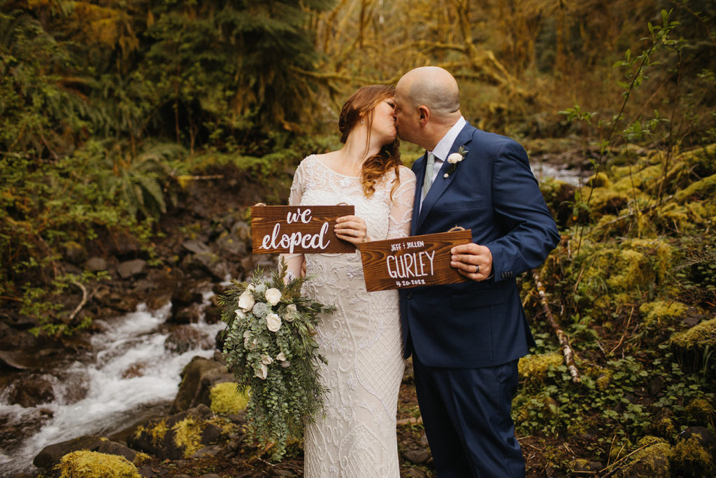 rain forest elopement bride and groom holding signs that say we eloped and their names and wedding date
