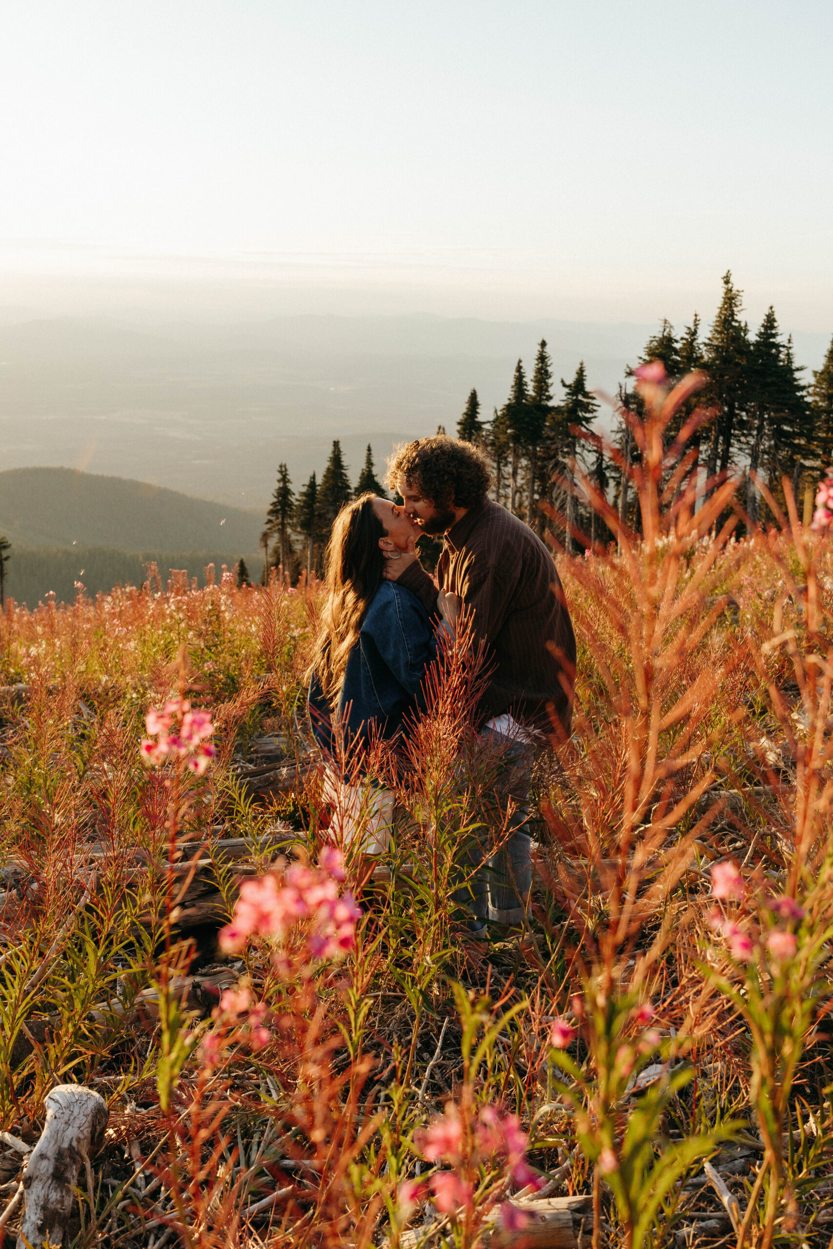 couple kissing in field of flowers for engagement session at sunset